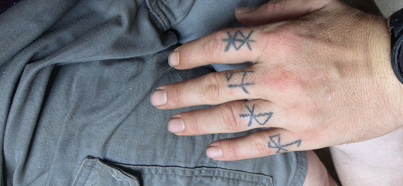 Fine-line symbols tattooed across fingers